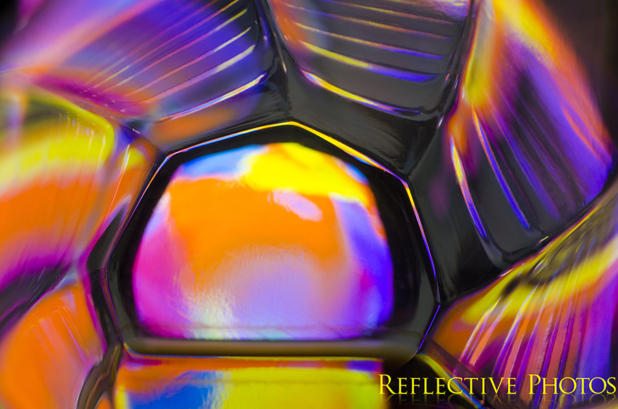 Neon colors make up this sunrise resembling photograph. An abstract painting shines through the bottom of a glass and creates colorful reflections along the ridged sides.